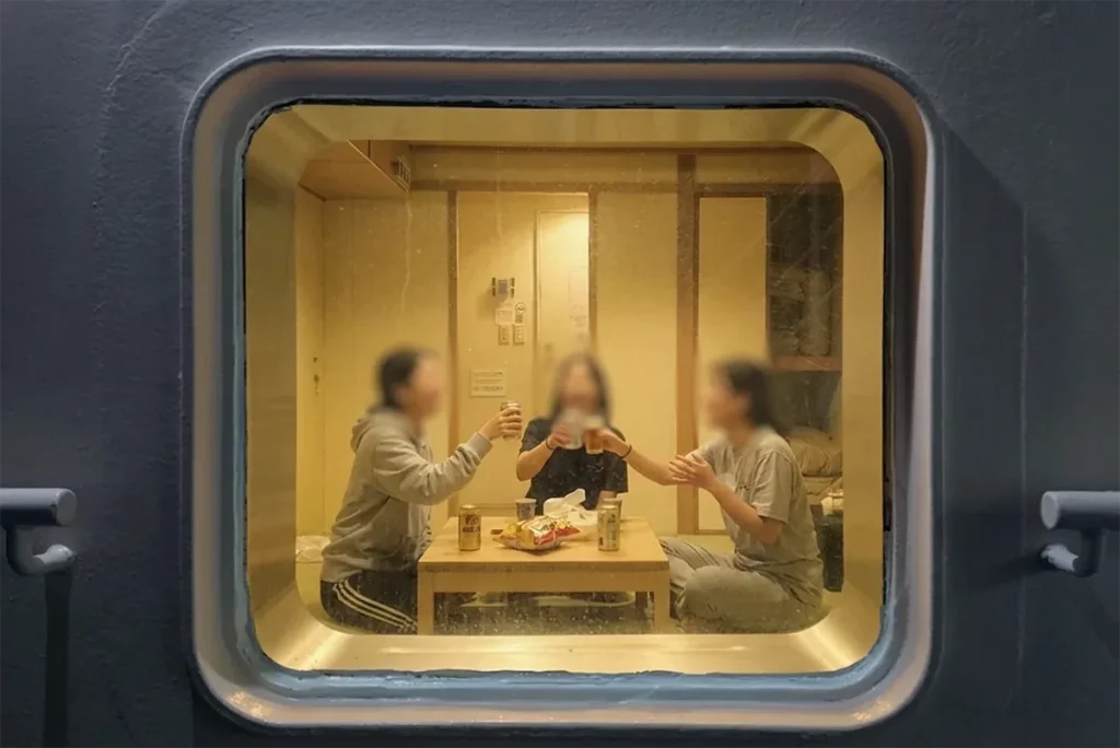 뉴카멜리아호 선실 안에서 세 명의 여행객이 중앙 테이블에 둘러앉아 캔맥주와 간식을 즐기며 즐겁게 건배하는 실제 이용 모습.